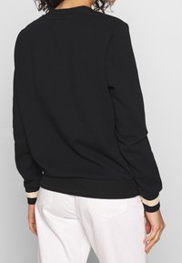 Czarna bluza z prążkowanym dekoltem i mankietami, z poziomymi beżowymi paskami. Miękka tkanina, luźny krój, ściągacz w pasie.