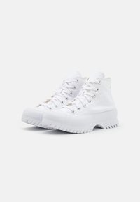 Zapatillas altas blancas con parte superior de lona suave, punta redonda, ojales de metal y suela de goma gruesa con textura acanalada.