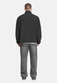 Czarna lekka kurtka z wysokim kołnierzem, widziana od tyłu. Sparowana z luźnymi szarymi dżinsami. Prosty design, bez widocznych wzorów ani akcentów.