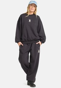 Sweatshirt oversize nero e pantaloni abbinati, entrambi in cotone, con dettaglio del logo. Abbinati a un cappellino azzurro e stivali neri.