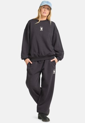 Sweatshirt oversize nero e pantaloni abbinati, entrambi in cotone, con dettaglio del logo. Abbinati a un cappellino azzurro e stivali neri.