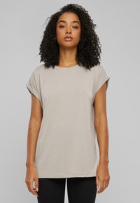 Ljust beige grundläggande t-shirt med upprullade korta ärmar, rund halsringning och mjukt tyg. Rakt snitt och minimal sömdetalj.