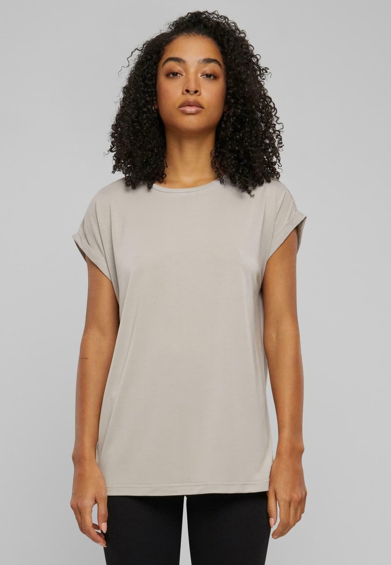 Ljust beige grundläggande t-shirt med upprullade korta ärmar, rund halsringning och mjukt tyg. Rakt snitt och minimal sömdetalj.