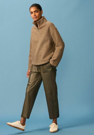 Brun fleece halv-zip pullover med en tekstureret overflade, parret med olivengrønne læderbukser og hvide sneakers. Enkel, lige snit.