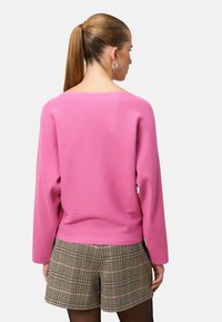 Pull côtelé rose à manches longues, associé à un short à carreaux. La texture semble douce et la coupe est décontractée avec un col large.