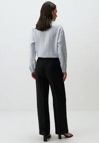 Lichtblauw linnen shirt met een ontspannen pasvorm en knoopdetails, gecombineerd met zwarte broek met elastische taille. Vlotte texturen, minimalistisch ontwerp.