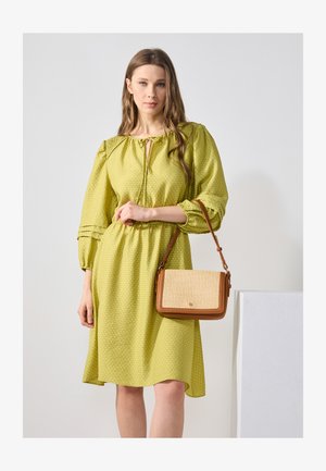 Limonkowa sukienka o teksturowanym wzorze, z puffami na rękawach i dekoltem z możliwością regulacji. Brązowa torebka z plecionym przodem i regulowanym paskiem.