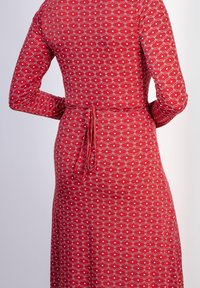 Punainen mekko, jossa on pitkät hihat, hyvin määritelty vyötärö soljella ja valkoinen aaltoilu kuvio, jossa on pisteitä kankaassa.
