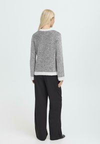 Hall sööburett ja valge triibuline kudum, ümmarguse kaeluse ja sooniku tekstuuriga, kontrastsete äärega, koos lahtiste mustade pükstega.