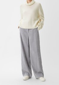 Stickad cremefärgad tröja med uppvikt krage, kombinerad med vida grå manchesterbyxor med vertikala ränder och vita sneakers.