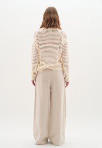 cremefarbener Strickpullover mit großem offenem Maschenmuster, gerippten Bündchen und Saum, kombiniert mit hellbeigen, weit geschnittenen Leinenhosen.