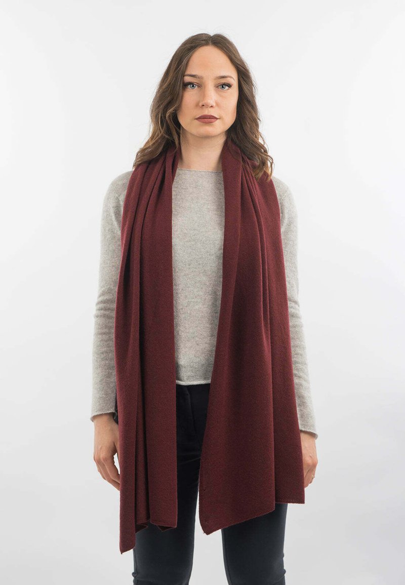 Burgundy šála, měkká textura, mírně splývající design, nošena přes světle šedý svetr, s volným střihem a dlouhými konci.