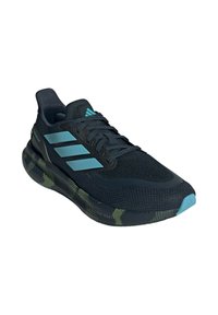 Chaussure de sport noire avec une tige en mesh respirant, accents bleus, et une semelle texturée ornée de motifs verts et jaunes.
