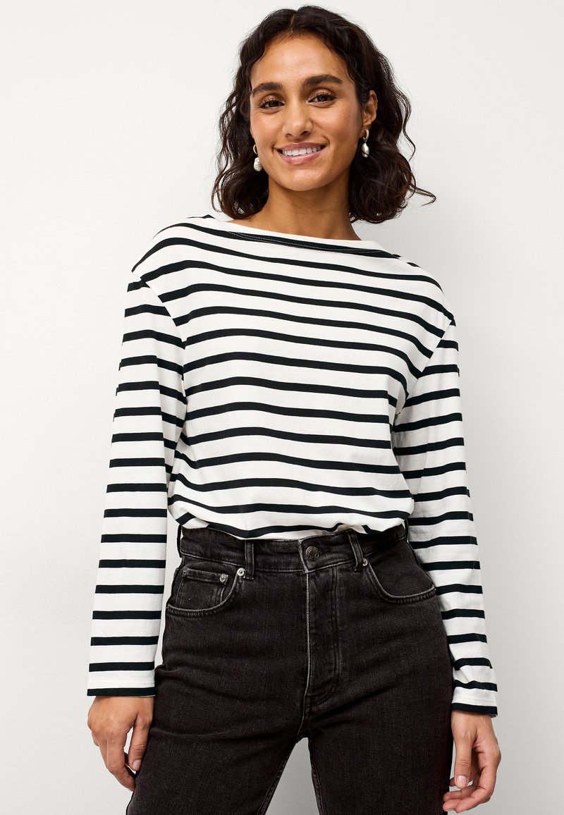 Zwart-wit gestreepte long-sleeve t-shirt met een bootnek, gecombineerd met hoge taille zwarte spijkerbroek. De stof lijkt zacht en ademend.
