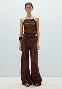 Brun texturerad tanktopp med volanger, kombinerad med burgundy vida byxor med vertikala vita ränder. Svart chunky armband och sandaler.