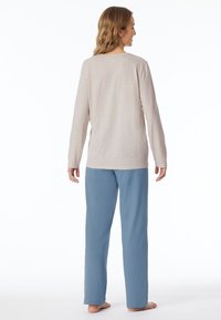 Leichtes Langarmshirt in sanftem Beige mit einem subtilen geometrischen Muster, kombiniert mit locker sitzenden, hellblauen Hosen. Beide sind im Relaxed Fit.