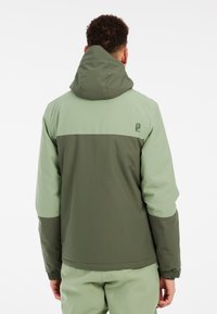 Grüne und khakifarbene Zip-Jacke mit Kapuze. Verfügt über ein Farbblockdesign, elastische Bündchen und ein Logo auf dem oberen Rücken. Glatte Textur.