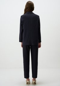 Giacca di abito a righe sottili blu navy con colletto a punte e maniche lunghe, abbinata a pantaloni coordinati. La texture del tessuto è liscia e su misura.
