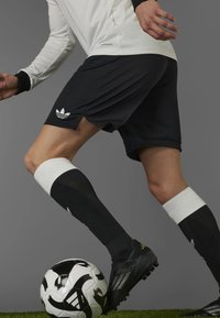 Black Adidas soccer shorts with white accents, paired with black and white knee-high socks, and a black and white soccer ball, on grass.