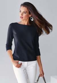 Marineblaues Oberteil mit drei Viertelärmeln aus einem glatten Material, kombiniert mit weißen Hosen, mit rundem Ausschnitt und minimalistischem Design.