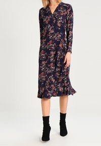 Navyblaues Blumenkleid mit Wickeldesign, langen Ärmeln und Rüschensaum. Verfügt über lebhafte Blumenmuster in Rot- und Grüntönen.