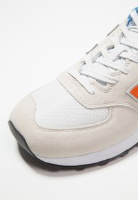 Baskets de sport gris clair avec un mélange de daim et de maille, dotées de lacets blancs et d'une accent orange. Embout arrondi et semelle texturée.