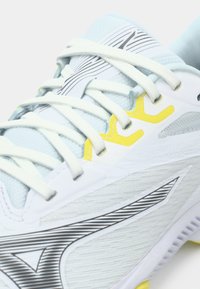 Light blue athletic shoe with white overlays, yellow accents, and textured detailing. Features thin white laces and sleek black stripes.