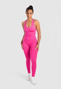 Mono rosa ajustado con escote redondo y tirantes gruesos, hecho de material elástico. Combinado con zapatillas deportivas blancas.