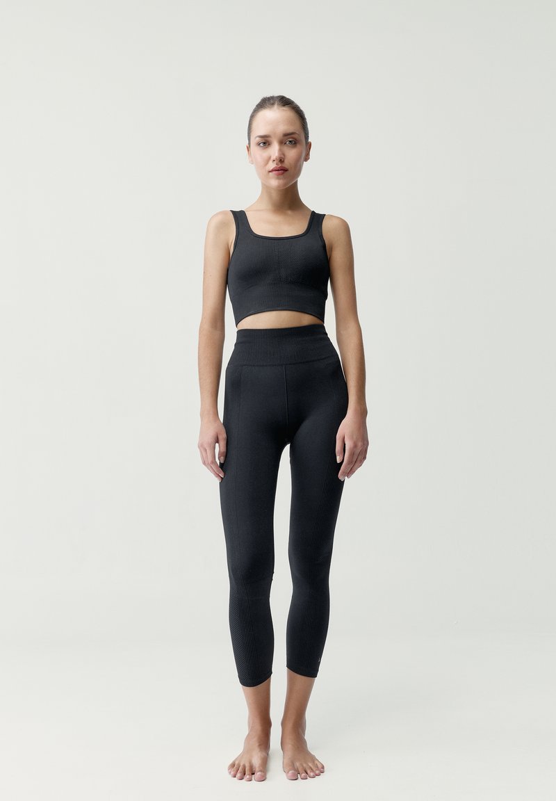 Čierny rebrovaný crop top a set legín s vysokým pásom, ktorý sa vyznačuje priliehavým strihom a dĺžkou po členky. Hladká textúra, minimálne detaily.