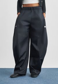 Fekete, bőszárú nadrág könnyű anyagból, elasztikus derékpánttal, oldalzsebekkel és egy kis logóval a bal zseb közelében.