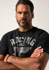 Černé bavlněné tričko s poškozeným bílým potiskem s nápisem "RACING LEAGUE." Kolo výstřih, krátké rukávy a volný střih.