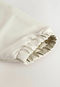 Poignet en tissu beige clair avec un élastique froncé et un léger éclat, présentant un motif de grille subtil sur une texture lisse.