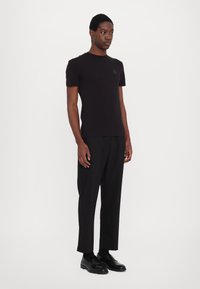 Tricou scurt negru cu guler rotund, având o etichetă logo discretă pe piept, asortat cu pantaloni negri pe măsură și încălțăminte.