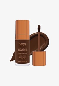 Correcteur liquide brun dans un contenant opaque avec un couvercle couleur cuivre. Comprend un applicateur en forme d'œuf et un échantillon du produit.