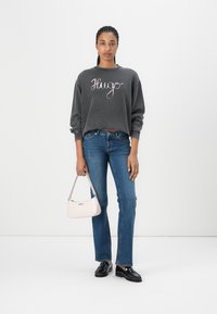 Gray sweatshirt with "Hugo" lettering, blue jeans, and black loafers. Carrying a light pink handbag with a curved design.