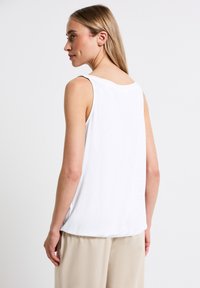 Top blanco sin mangas de tela suave, con un escote redondo y un corte relajado, combinado con pantalones beige para un look informal.