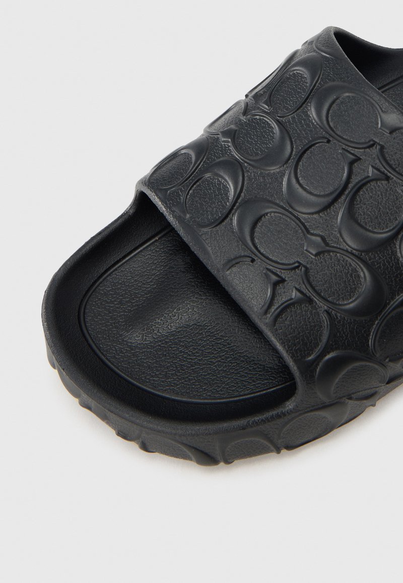 Schwarze Slidesandale mit einer strukturierten Gummi-Oberfläche mit kreisförmigem Muster, konturiertem Fußbett und leicht erhöhtem Absatz.