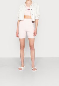 Ljusrosa, figursydd crop top och högmidjade shorts, tillsammans med en vit denimjacka och vita sandaler. Har varumärkesdetaljer på kläderna.