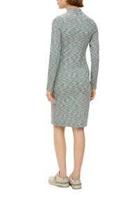 Sukienka z długim rękawem w heatherowym zielonym kolorze, w dopasowanym kroju, sięgająca do połowy łydki. Posiada wysoki dekolt i jest zestawiona z jasnymi trampkami.