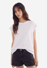 Hvid bomulds t-shirt med korte ærmer og øjenlåg detaljering. Parret med sorte denim shorts med en frynset kant.