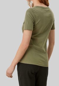 Oliven grønn kortærmet t-shirt med rund halsudskæring, tætsiddende silhuet, glat tekstur og minimale syningsdetaljer, kombineret med sorte bukser.