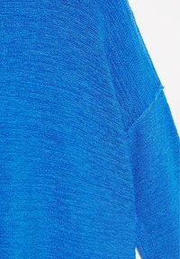 Gros plan d’un tissu tricoté bleu montrant une texture détaillée et des coutures le long d’une couture.