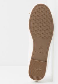 Semelle extérieure en caoutchouc marron d'une chaussure blanche avec surface texturée antidérapante, étiquette anti-dérapante, taille de chaussure 37 et nom de marque "Tamaris" visible.