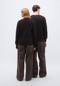 Pulls sombres en tricot avec ourlets côtelés, associés à des pantalons amples marron. Vêtements texturés mis en valeur sur un fond clair.