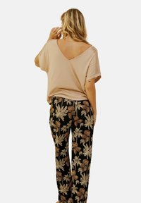 Haut beige clair avec un col en V et des détails en dentelle sur les manches, associé à un pantalon noir avec de grands motifs floraux dans des tons crème et or.