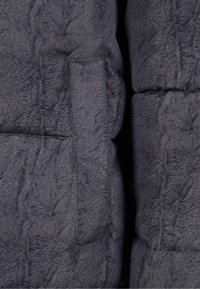 Kviltad mörkgrå jacka med en strukturerad yta, med en sidoficka och synlig sömdetalj. Kompakt och fluffig design.