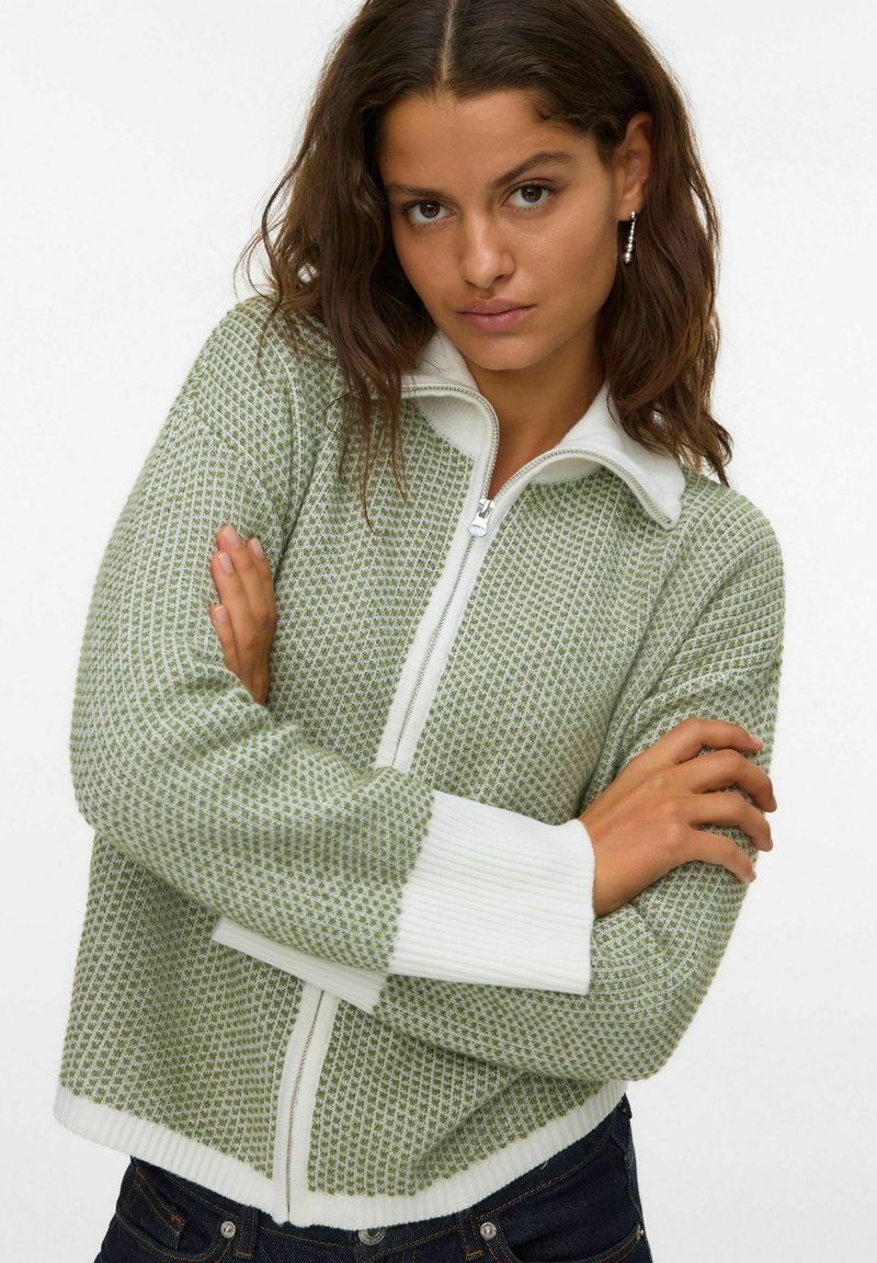 Zielony sweter na zamek z dzianiny, z białymi prążkowanymi mankietami i kołnierzykiem, wyróżniający się teksturowanym wzorem i skróconym fasonem.