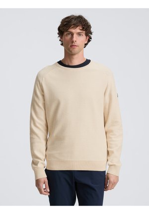 Pull en tricot beige à col rond avec des cuffs et un ourlet côtelés, présentant un accent bleu marine foncé au col et une texture subtile sur l'ensemble.