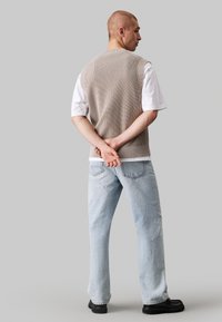 Maglione beige a maglia sopra una t-shirt bianca, abbinato a jeans azzurri a gamba dritta e scarpe nere, visto da dietro.