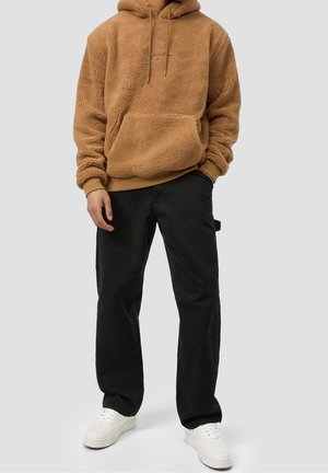 Brauner Fleece-Hoodie mit Kängurutasche und Kapuze mit Kordelzug, kombiniert mit schwarzen Cargo-Hosen und weißen Sneakers.